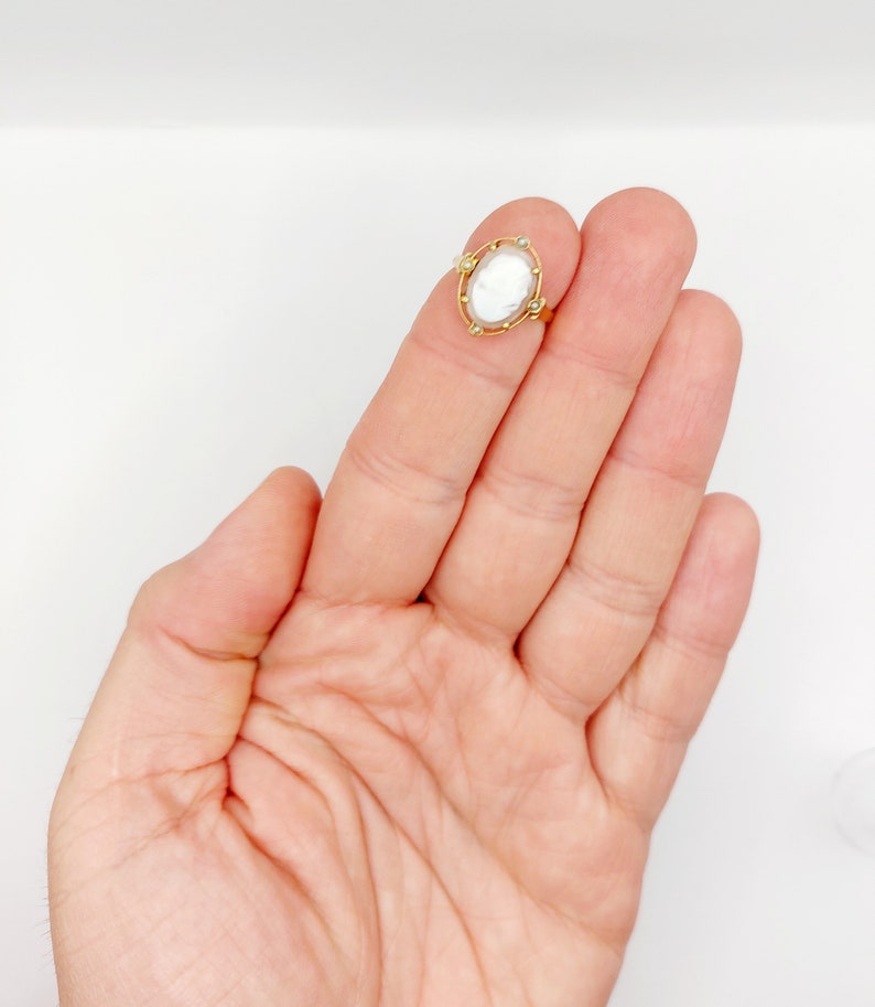 May include: A gold ring with a white cameo set in a gold frame with small gold beads around the edge.
