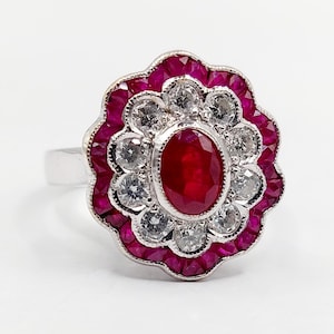 Peut inclure: Bague en argent ornée d'un rubis ovale central, entouré de diamants et d'une bordure de petits rubis. La bague présente un motif floral aux couleurs rouge vif et blanc.