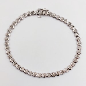 Peut inclure: Un bracelet en argent orné d'une série de pierres précieuses rondes et transparentes, serties dans des chatons individuels. Le bracelet présente un design classique avec un fermoir sécurisé. Les pierres sont espacées uniformément.