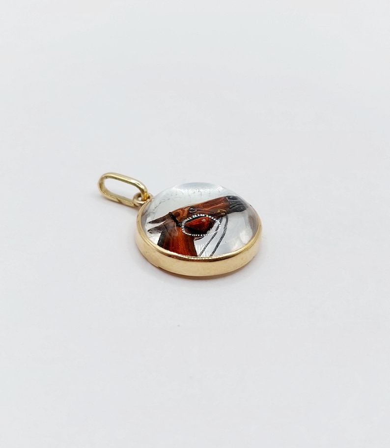 May include: A gold pendant with a clear glass cabochon featuring a painted image of a horse's head.