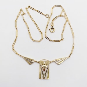 May include: A gold-tone necklace featuring a delicate chain with elongated rectangular links and a central pendant. The pendant consists of a rectangular frame with geometric cutouts and two matching triangular side accents in yellow and white metal.