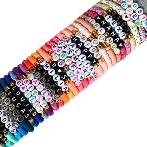 May include: A stack of colourful beaded bracelets with different names spelled out on them. The bracelets are made of silicone and have gold accents. The names on the bracelets include:  "OUSIN", "MCREW", "TEXT", "NANA", "GIRLSMO", "BRIDE", "CHAPPY", "MAALIYAH", "JASMINET", "BFF", "BIGOSIS", "GEMOLIA", "CHLOE", "RUNCLUB", "CLAYLAD", "ESISSY", "MBAILEY", "CLOUIE", "CLUCAS", "GRANT", "DAM", "ONG", "N", "A".