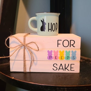 May include: A light green ceramic mug with a black bunny silhouette and the word "HOP" sits atop three white wooden blocks tied with twine. The blocks read "FOR PEEPS SAKE" with colorful bunny graphics.