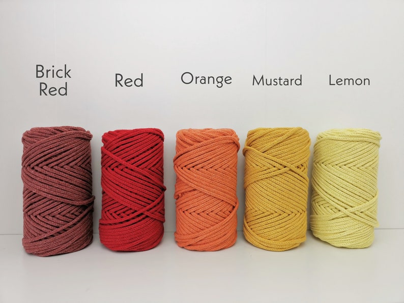 K&ouml;nnte beinhalten: F&uuml;nf Spulen Baumwollseil in verschiedenen Rot-, Orange- und Gelbt&ouml;nen. Die Farben sind mit "Brick Red", "Red", "Orange", "Mustard" und "Lemon" beschriftet.