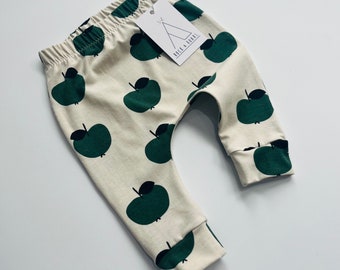 May include: Cream colored baby leggings with a green apple print. The leggings have a tag that says "Rock & Roar's".