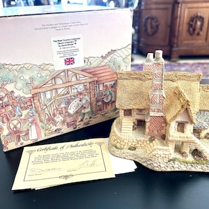 May include: A detailed miniature cottage figurine with a thatched roof, brick chimneys, and stone foundation. The figurine is part of "The West Country Collection" by David Winter. A box and certificate of authenticity are also present.