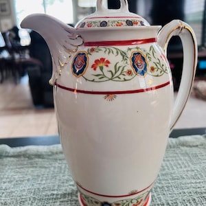 May include: White porcelain teapot with a red, gold, and blue floral design. The teapot has a lid and a handle.
