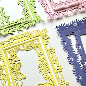 May include: Four decorative paper frames with intricate cut-out designs. The frames are in shades of green, pink, yellow, and purple.