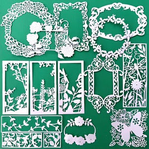 May include: A collection of white die-cut paper shapes featuring intricate floral, butterfly, dragonfly, and ornate frame designs. These delicate, laser-cut embellishments showcase various botanical patterns, rectangular borders, and circular wreaths.