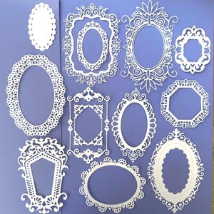 May include: A selection of white, intricately designed oval and geometric frames on a purple background. The frames vary in size and style, featuring delicate lace-like patterns and ornate details, ideal for crafting or scrapbooking projects.