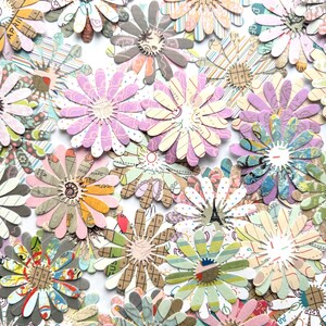 May include: A selection of colourful paper daisy flowers with patterned petals and textured centres. The flowers are in various colours, including pink, green, and yellow, and are arranged on a white background. The flowers appear to be handmade.