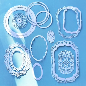 May include: A collection of white metal die-cut shapes featuring various intricate frames, borders, and decorative medallions. The set includes circular, oval, and rectangular outlines with ornate filigree patterns and scalloped edges.