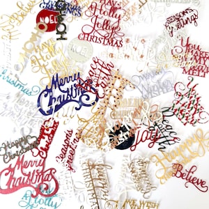 May include: A collection of assorted holiday-themed die-cut paper phrases and words in various colors including red, gold, blue, and white. The text includes phrases such as Merry Christmas, Holly Jolly, Peace on Earth, Believe, Joy, and Season's Greetings.