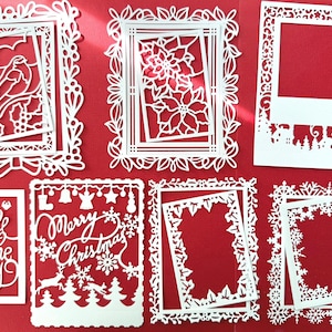May include: White paper cutouts with Christmas and winter themes, including frames, a poinsettia, a bird, and the phrases "Jingle all the way" and "Merry Christmas". The cutouts are on a red background.
