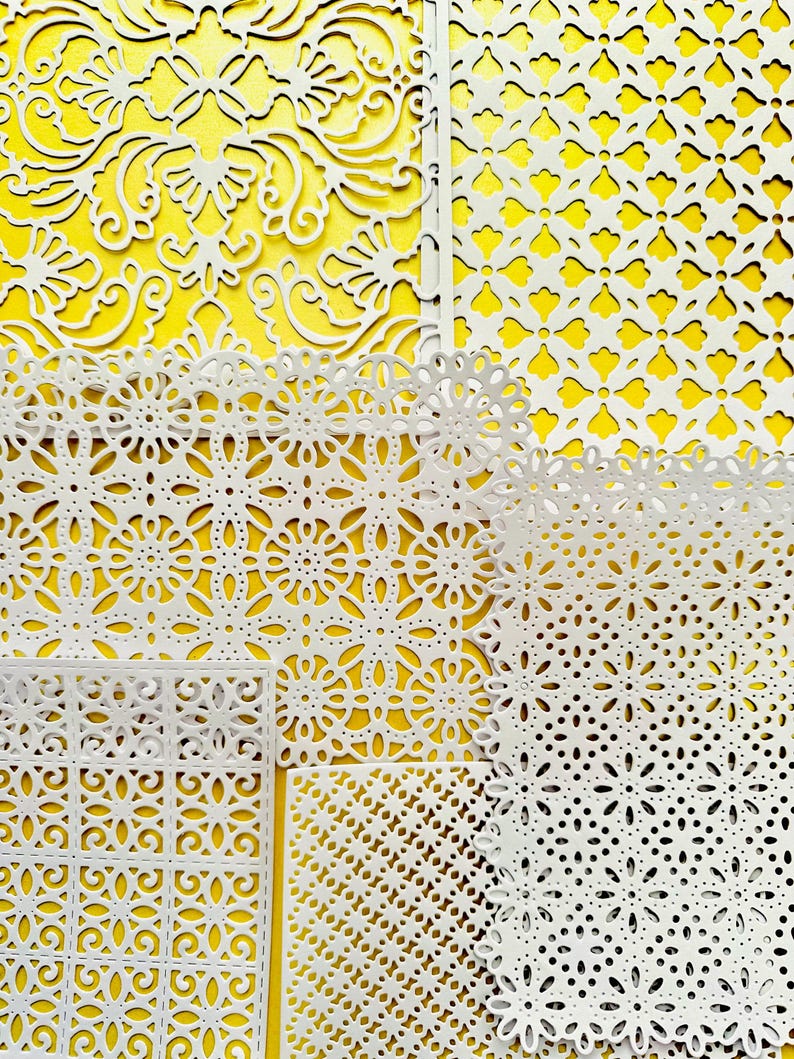 K&ouml;nnte beinhalten: Ein Satz von sechs wei&szlig;en, lasergeschnittenen Papierschablonen mit komplizierten geometrischen Mustern. Die Schablonen sind auf einem gelben Hintergrund angeordnet.