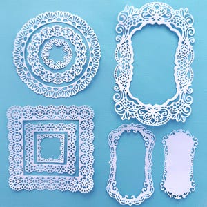 May include: A collection of white paper die-cut shapes featuring intricate lace-like patterns. The set includes three circular frames, three square frames, two rectangular ornate frames, and one solid rectangular label with decorative edges.