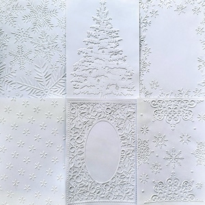 May include: A collection of six white rectangular cards featuring embossed designs. The patterns include a field of snowflakes, a central Christmas tree, a snowflake border, a small snowflake pattern, an oval frame with holly, and ornate snowflakes.