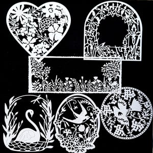 May include: A set of six white paper cutouts featuring floral and bird designs. The designs include a heart, a rectangle, a circle, and two arches. The cutouts are intricate and delicate, with a variety of floral patterns and birds.