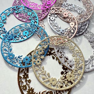 May include: An assortment of oval-shaped, glitter-covered floral cutouts in shades of gold, silver, pink, blue, and bronze. The cutouts showcase detailed floral and leaf patterns, offering a delicate and decorative aesthetic. These embellishments are suitable for crafting and creative projects.
