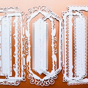 Può includere: Set di otto cornici decorative in carta bianca con disegni intricati. Le cornici sono sovrapposte e annidate l'una nell'altra, creando un effetto multidimensionale.