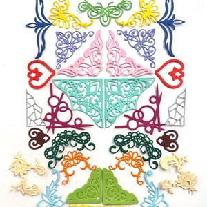 May include: A selection of colourful, die-cut paper embellishments in various shapes and sizes. The assortment includes floral, corner, and decorative designs in shades of blue, green, yellow, pink, and orange. These craft supplies are ideal for scrapbooking and card making.