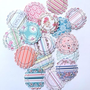 May include: A collection of circular paper doilies featuring a variety of patterns including floral prints, stripes, and damask designs in shades of pink, blue, green, and white. Each doily has a decorative scalloped edge with intricate die-cut holes.