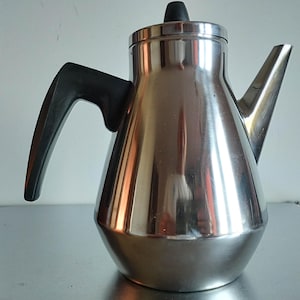 May include: A polished stainless steel coffee pot with a tapered body, a wide base, and a curved spout. The pot features a black plastic handle attached to the side and a matching black knob on the lid, providing a functional design for brewing.