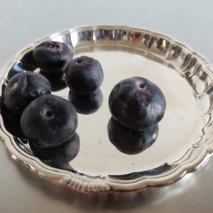 Puede incluir: Un plato de servir plateado con un borde festoneado, que contiene cinco arándanos azules oscuros.