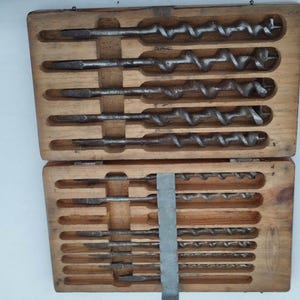 Puede incluir: Un juego de brocas en una caja de madera. Las brocas están dispuestas en filas y todas son del mismo tamaño. La caja está hecha de madera y tiene una tapa con bisagras.