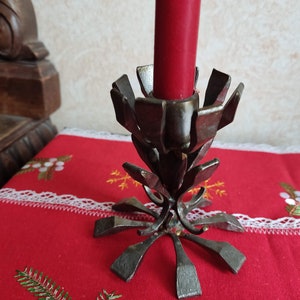 May include: A silver metal candle holder with a unique design resembling a flower. The holder has a wide base with six points and a central stem that rises to a cup-shaped top. A red candle is placed in the top.