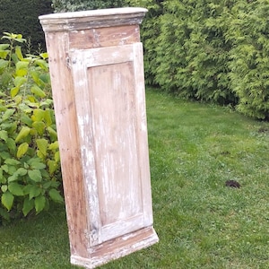 May include: A white painted wooden corner cabinet with a single door. The cabinet is standing on a grassy lawn.