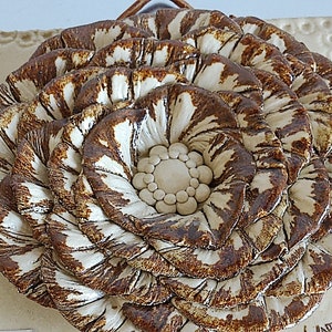 May include: A ceramic flower wall decor with brown and white glaze. The flower has a layered design with a center circle.