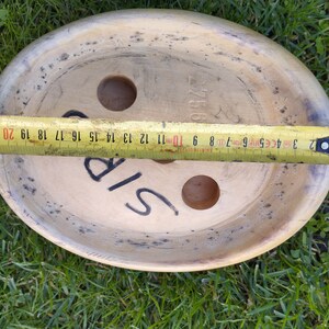 May include: A round, wooden, light brown disc with two holes and the word "SIP" written on it. The disc is 20 inches in diameter.