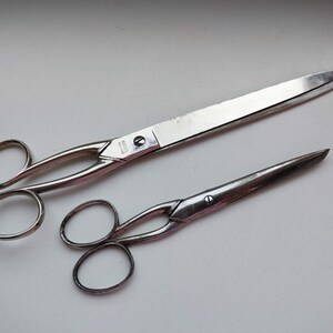 May include: Two pairs of silver scissors. The larger pair has a handle with a small hole and the words "Made in England" on the blade. The smaller pair has a more rounded handle.