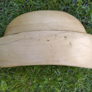 May include: A light brown wooden hat form, used for shaping hats during the millinery process. The form is smooth and has a rounded crown and a wide brim.