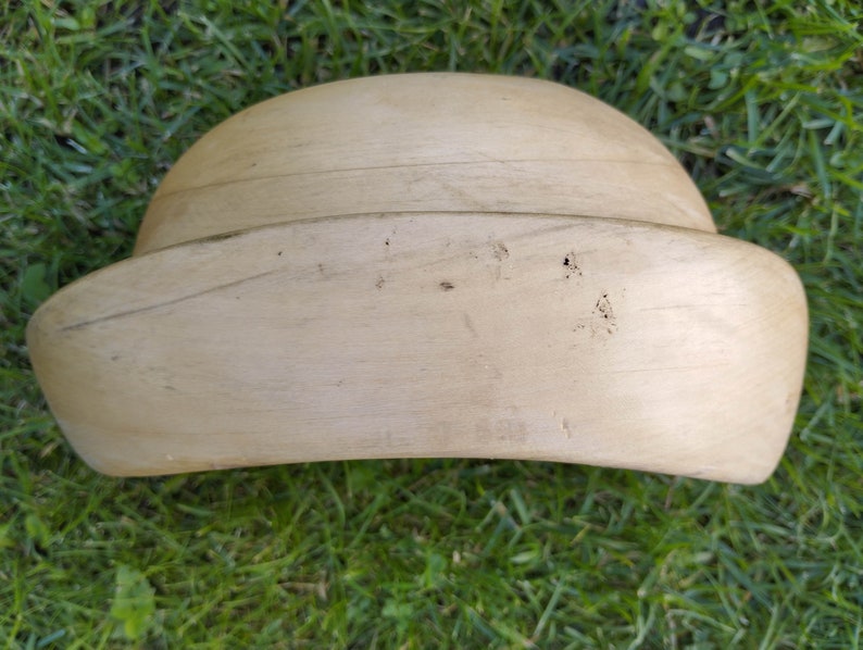 May include: A light brown wooden hat form, used for shaping hats during the millinery process. The form is smooth and has a rounded crown and a wide brim.