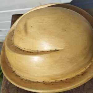 May include: A wooden bowl with a light brown finish. The bowl has a rounded shape and a wide rim.