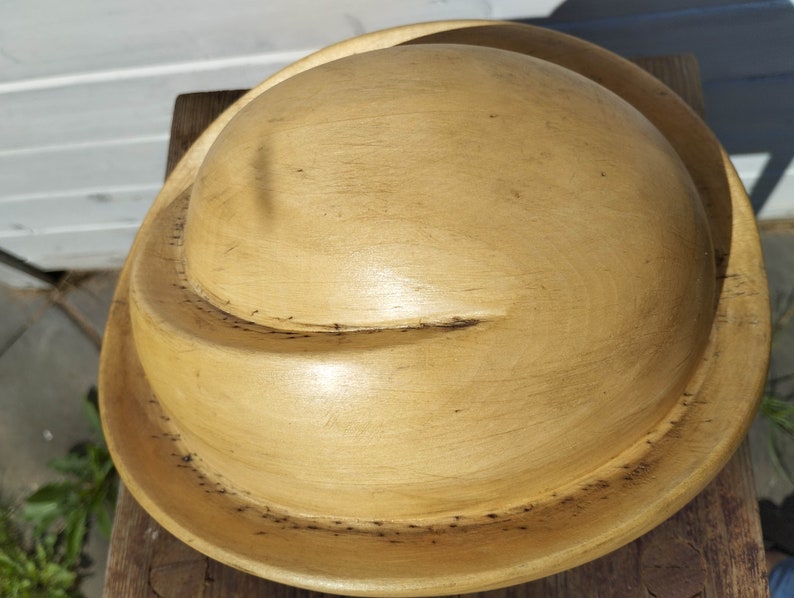 May include: A wooden bowl with a light brown finish. The bowl has a rounded shape and a wide rim.