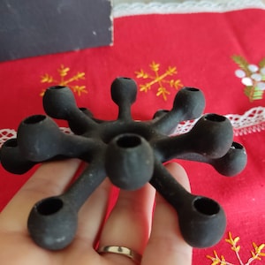 Puede incluir: Candelero de metal negro con diseño de estrella y nueve portavelas.