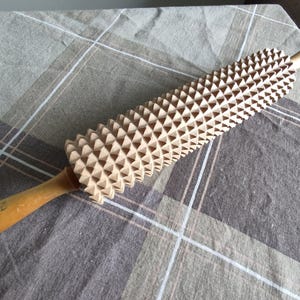 Könnte beinhalten: Ein Nudelholz aus Holz mit einer strukturierten Oberfläche aus dreieckigen Spitzen. Das Nudelholz ist braun und hat einen Holzgriff.