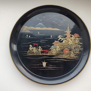 Könnte beinhalten: Ein schwarzes Lacktablett mit einem goldenen und roten japanischen Landschaftsdesign. Das Tablett zeigt einen Berg, eine Pagode, eine Brücke und ein Boot. Das Design ist aufwendig und detailliert.