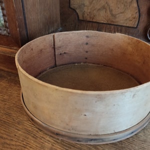 Op de afbeelding: Een houten bloemzeef met een gaaszeef erin. De zeef is rond en heeft een diameter van ongeveer 25 cm.