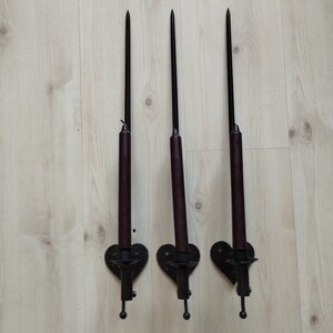 Pode incluir: Três castiçais de parede de metal preto com velas marrons. Os castiçais têm a forma de um coração e um design decorativo.