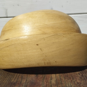 May include: A wooden hat block, a tool used by milliners to shape hats, is made of light brown wood and has a rounded top and a wide brim.
