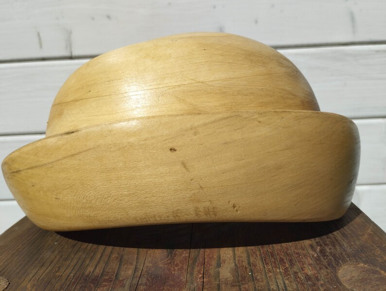 May include: A wooden hat block, a tool used by milliners to shape hats, is made of light brown wood and has a rounded top and a wide brim.