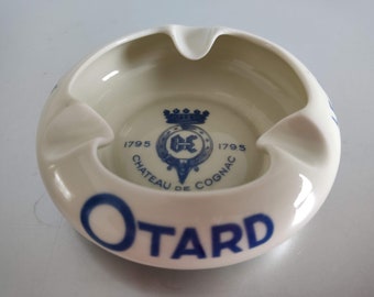 May include: White ceramic ashtray with a blue and white logo for Chateau de Cognac Otard, established in 1795.