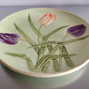 May include: A ceramic plate with a green background and three raised tulips. The tulips are purple, pink, and white.