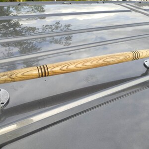 May include: A wooden handrail with a natural wood finish and metal end caps. The handrail is mounted on a gray surface.