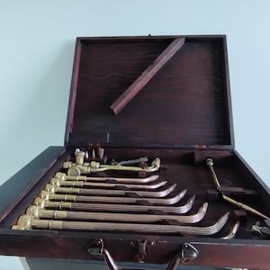 May include: A wooden carrying case with a brass latch, containing a set of welding torches. The case is open and the torches are arranged in rows.