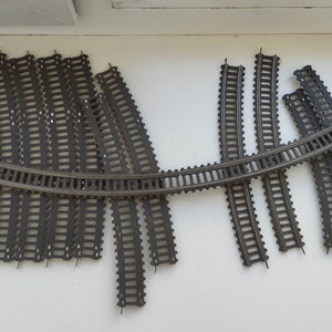 Puede incluir: Un conjunto de vías de tren modelo de plástico negro, que incluye piezas curvas y rectas. Las vías están dispuestas en una formación curva.